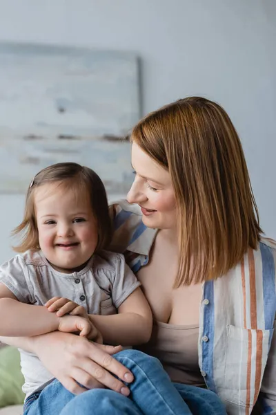 Lächelnde Mutter umarmt Tochter mit Down-Syndrom im Schlafzimmer — Stockfoto