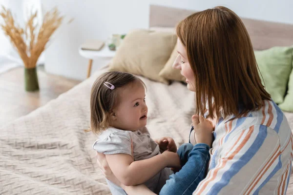 Mother playing with toddler daughter with down syndrome on blurred bed — Stock Photo