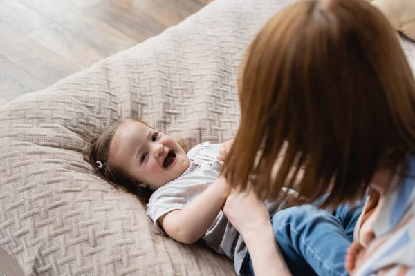 Vue en angle élevé de la femme jouant avec la fille gaie avec le syndrome du duvet sur le lit — Photo de stock