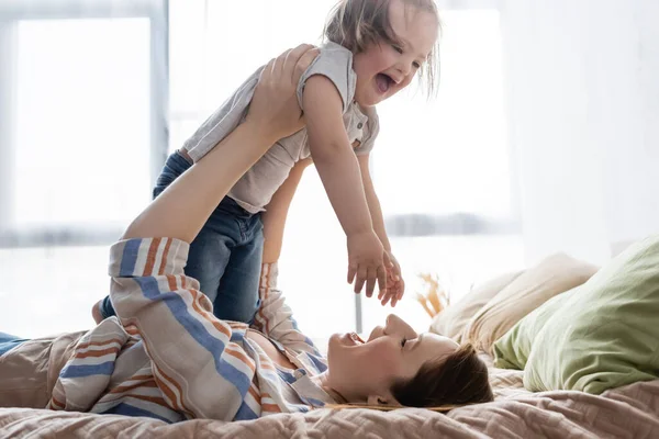 Femme heureuse tenant fille excitée avec le syndrome du duvet sur le lit — Photo de stock