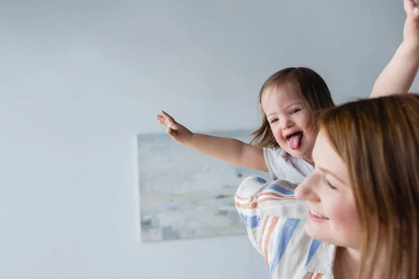 Enfant atteint du syndrome du duvet qui sort de la langue près d'une mère floue à la maison — Photo de stock