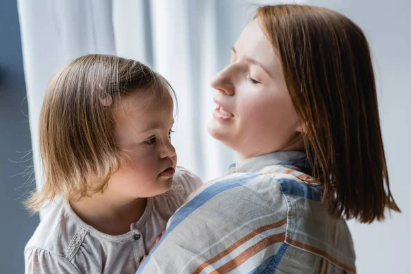 Toddler kid with down syndrome looking away near mother at home — Stock Photo