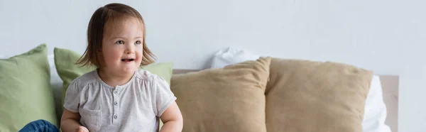 Smiling toddler girl with down syndrome looking away on bed, banner — Stock Photo