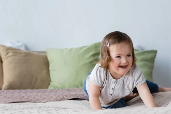 Niño feliz con síndrome de Down mirando hacia otro lado en la cama en casa - foto de stock