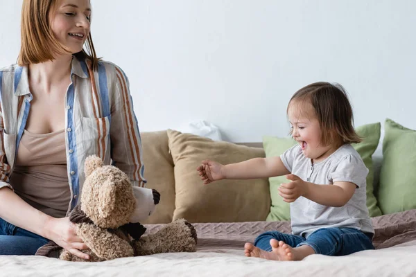 Pais segurando brinquedo macio perto da filha animada com síndrome de down na cama — Fotografia de Stock