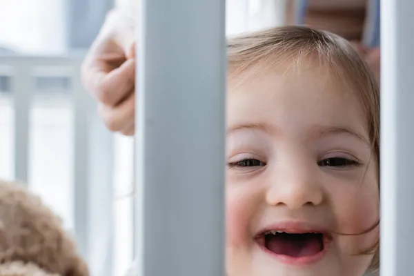 Child with down syndrome looking at camera in baby crib near blurred mother — Stock Photo