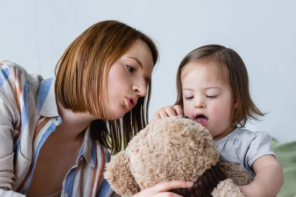 Mother talking to toddler daughter with down syndrome holding soft toy at home — Stock Photo