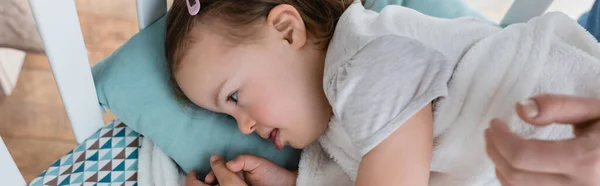 Seitenansicht eines Babys mit Down-Syndrom, das in der Krippe neben der Hand der Mutter liegt, Banner — Stockfoto