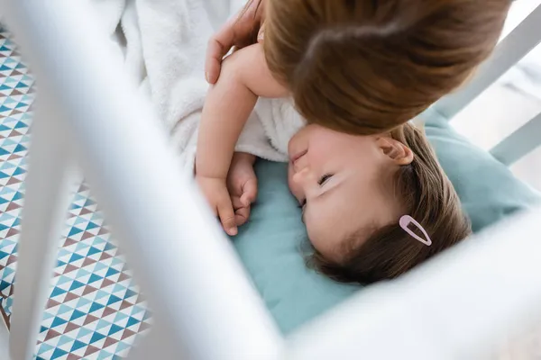 Vue aérienne de la mère touchant un enfant atteint du syndrome du duvet dans un berceau à la maison — Photo de stock