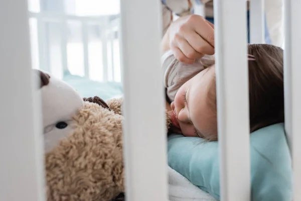 Parent touching sleeping daughter with down syndrome in crib at home — Stock Photo