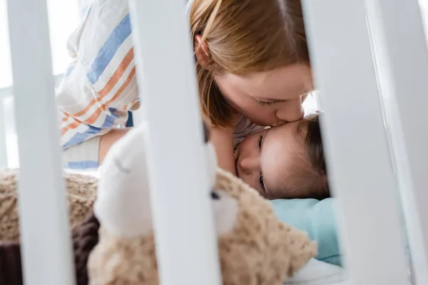 Mutter küsst Mädchen mit Down-Syndrom in der Nähe von Stofftier im Babybett — Stockfoto