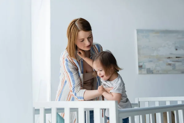 Mãe segurando bebê com síndrome de down perto berço em casa — Fotografia de Stock