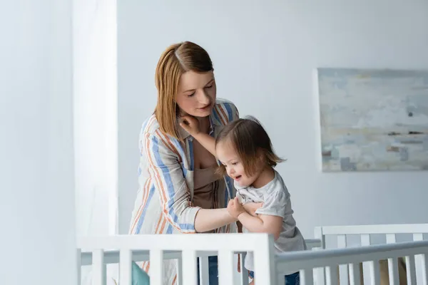 Madre che tiene il bambino con la sindrome di Down vicino culla a casa — Foto stock