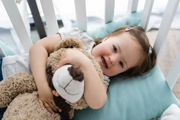 Вид зверху на дівчинку з синдромом Дауна, що обіймає м'яку іграшку в ліжечку — стокове фото