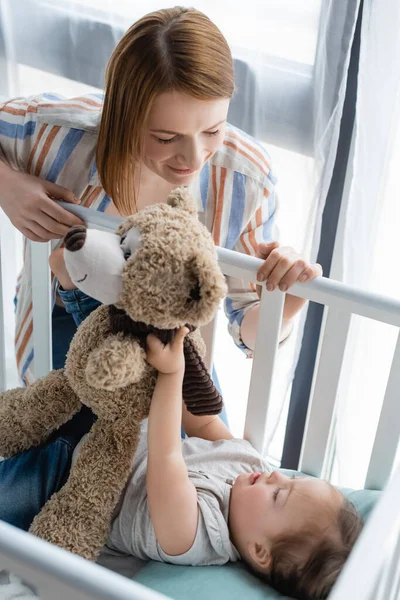 Mãe olhando para o bebê com síndrome de down segurando brinquedo macio no berço — Fotografia de Stock