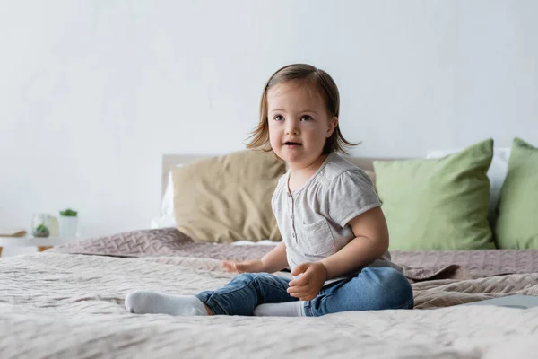 Positive child with down syndrome sitting on bed at home — Stock Photo