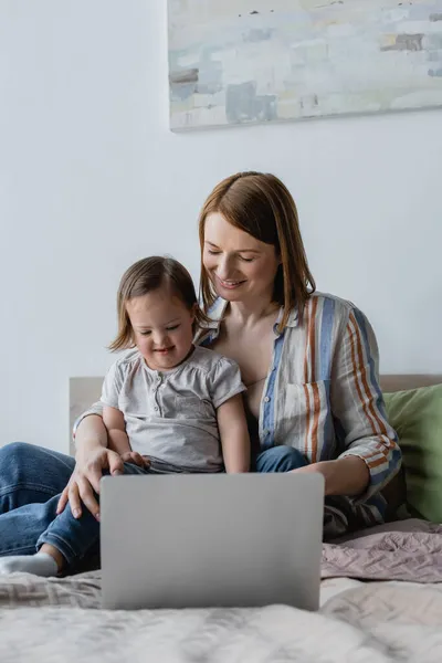 Mãe abraçando filha com síndrome de down perto de laptop na cama — Fotografia de Stock