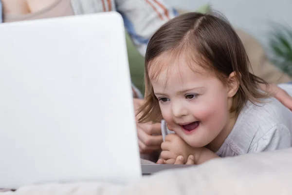 Niño emocionado con síndrome de Down mirando borrosa portátil cerca de la madre - foto de stock