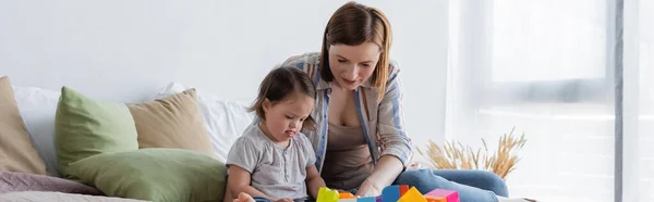 Parent jouant avec l'enfant avec le syndrome du duvet près des blocs de construction sur le lit, bannière — Photo de stock