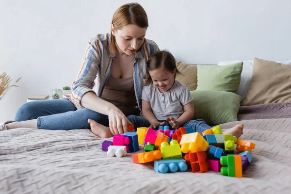 Mujer y niño con síndrome de Down jugando bloques de construcción en la cama en casa - foto de stock