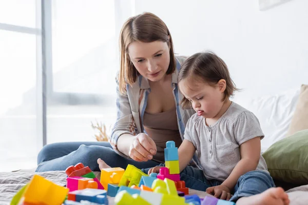 Eltern und Tochter mit Down-Syndrom spielen zu Hause Bausteine auf dem Bett — Stockfoto