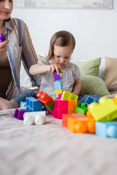 Girl with down syndrome playing building blocks on bed near mother — Stock Photo