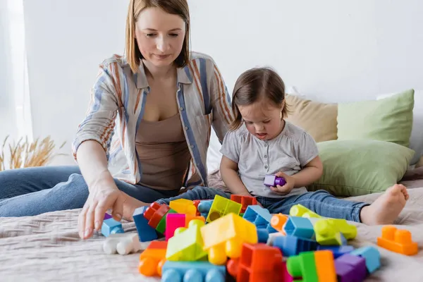 Eltern und Kind mit Down-Syndrom spielen zu Hause bunte Bausteine auf dem Bett — Stockfoto