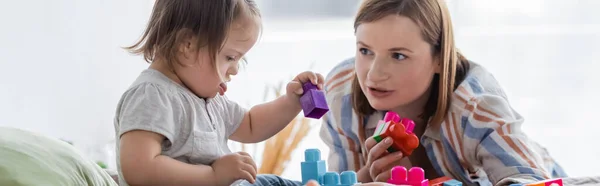 Mother talking to daughter with down syndrome playing building blocks at home, banner — Stock Photo