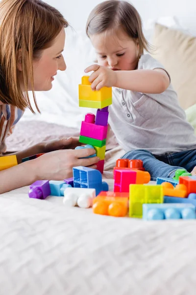 Happy woman looking at toddler child playing building blocks on bed — Stock Photo