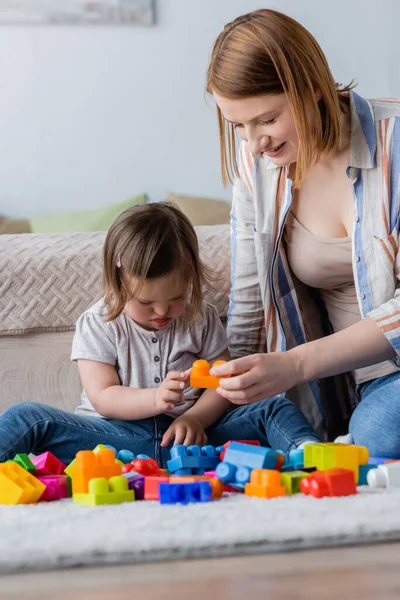 Woman playing building block with child with down syndrome on carpet in bedroom — Stock Photo