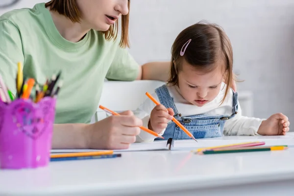 Parent sitting near daughter with down syndrome drawing on paper at home — Stock Photo