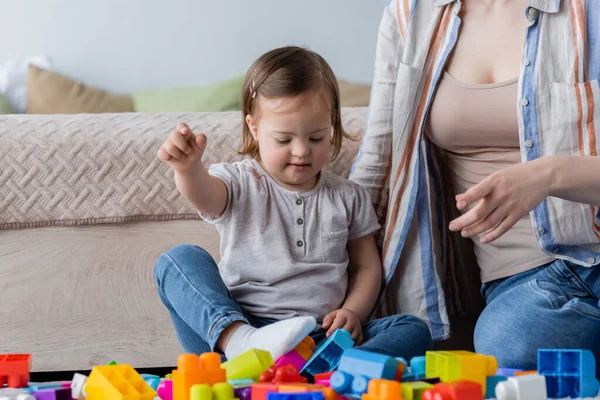 Bambino con sindrome di Down seduto vicino alla mamma e mattoni a casa — Foto stock