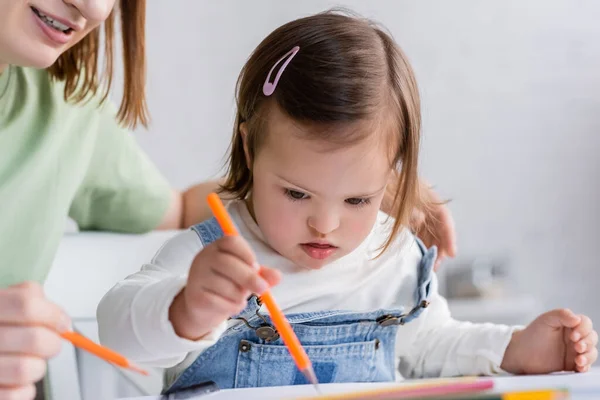 Femme souriante tenant crayon de couleur près de la fille avec le syndrome du duvet à la maison — Photo de stock