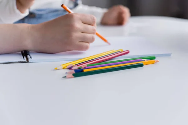 Vue recadrée de la femme dessinant près de l'enfant flou et crayons de couleur sur la table — Photo de stock