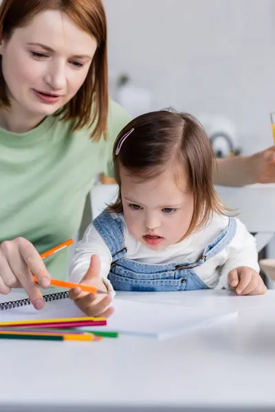 Pais segurando lápis de cor perto da filha com síndrome de down e papel na cozinha — Fotografia de Stock