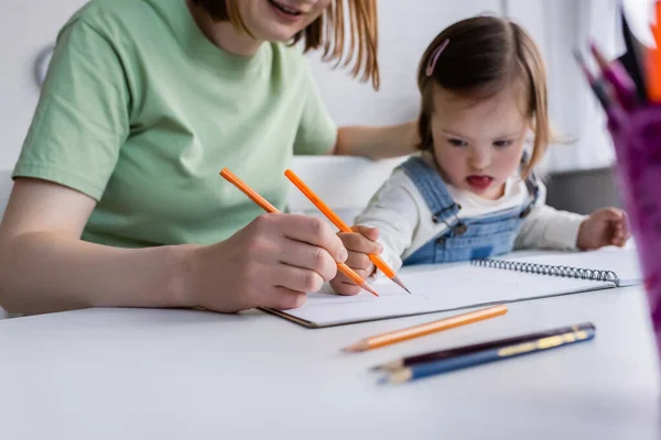 Blurred kid with down syndrome drawing on paper near mom in kitchen — Stock Photo