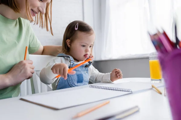 Maman étreignant tout-petit enfant avec le syndrome du duvet tenant crayon de couleur près du jus d'orange dans la cuisine — Photo de stock