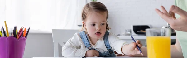 Kleinkind mit Down-Syndrom hält Farbstift in der Nähe von Orangensaft und Mama, Banner — Stockfoto