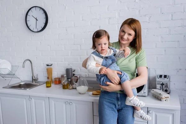 Parent holding child with down syndrome holding whisk in kitchen — Stock Photo