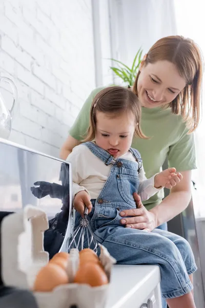 Genitore in piedi vicino a bambino con sindrome di Down tenendo frusta vicino alle uova in cucina — Foto stock