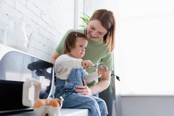 Щаслива мати, що стоїть біля дитини з синдромом Дауна та інгредієнтами на кухні — стокове фото
