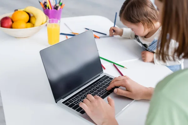 Mulher usando laptop perto da filha com síndrome de down desenho na cozinha — Fotografia de Stock