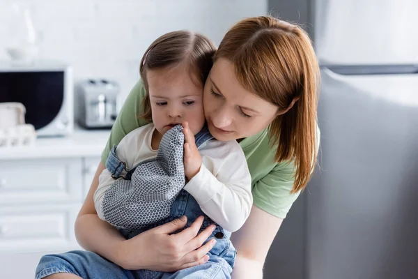 Mulher abraçando filha com síndrome de down na luva de cozimento na cozinha — Fotografia de Stock