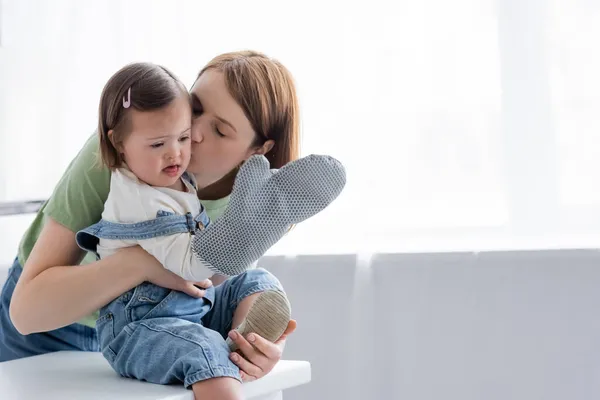 Батько цілує дитину з синдромом Дауна, тримаючи рукавичку для випічки на кухні — стокове фото