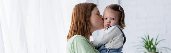 Женщина целует ребенка с синдромом Дауна дома, баннер — стоковое фото
