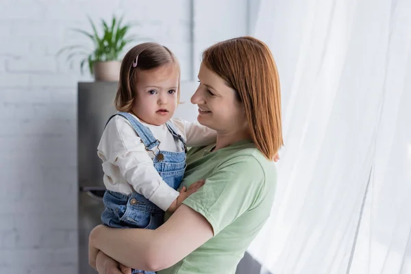 Улыбающаяся мама держит малыша с синдромом Дауна дома — стоковое фото