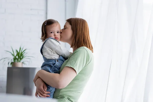 Мать целует ребенка с синдромом Дауна на кухне — стоковое фото