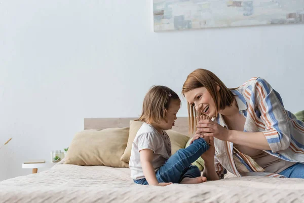 Woman holding feet of daughter with down syndrome on bed — Stock Photo