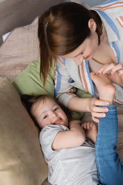 Vue grand angle de la femme touchant les pieds de l'enfant avec le syndrome du duvet sur le lit — Photo de stock