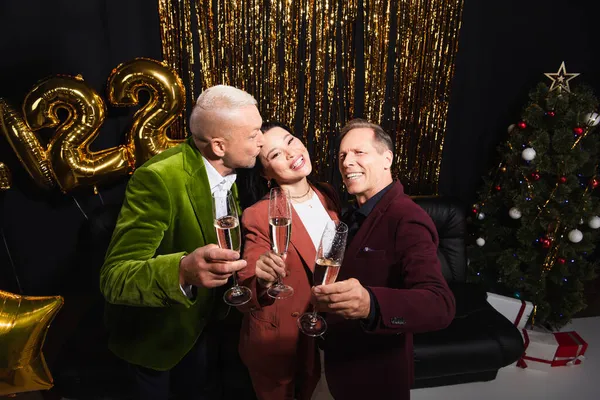 Sonrientes amigos maduros interracial celebración de champán mientras se celebra el año nuevo sobre fondo negro - foto de stock